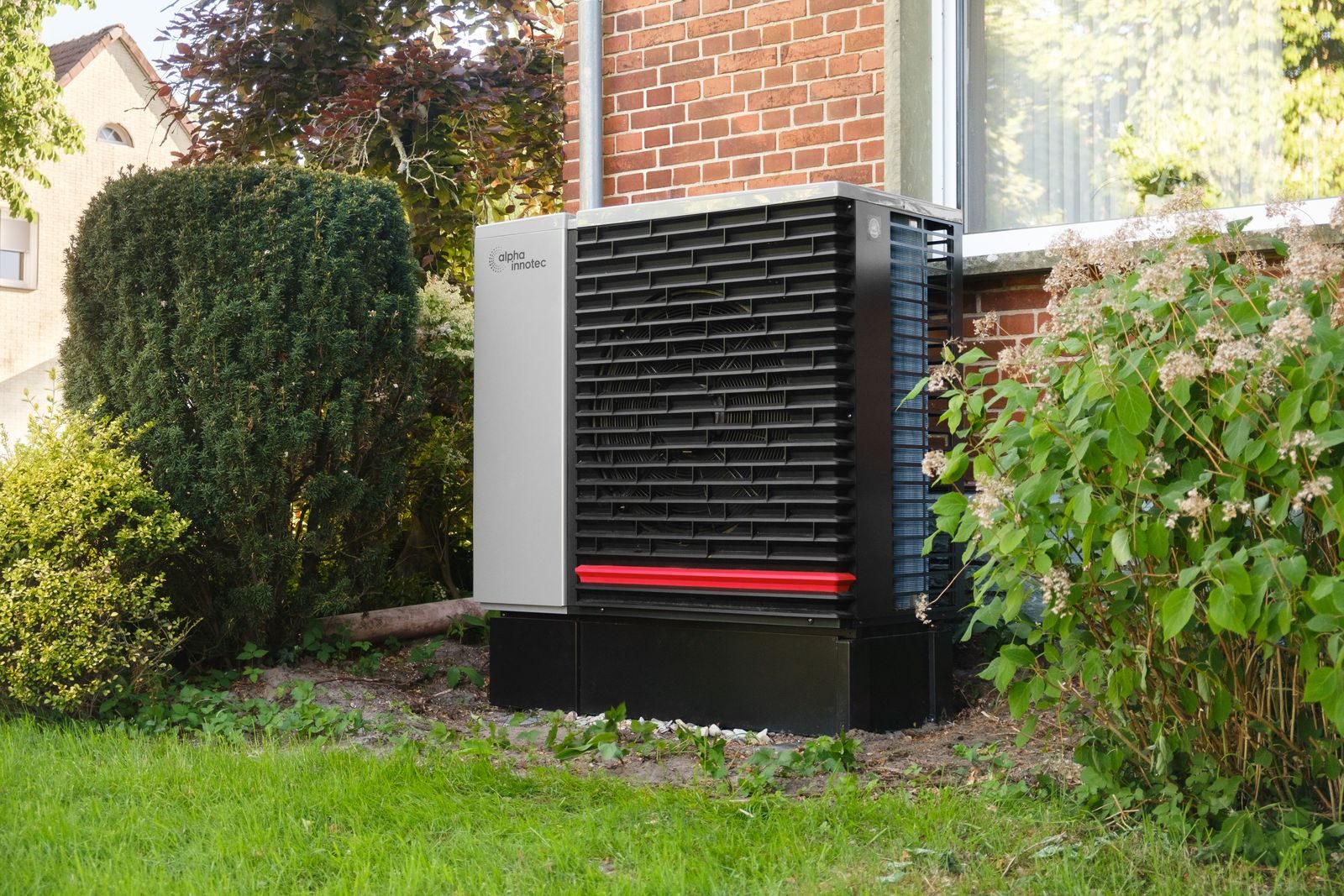 An air source heat pump standing on a plinth against an external wall.