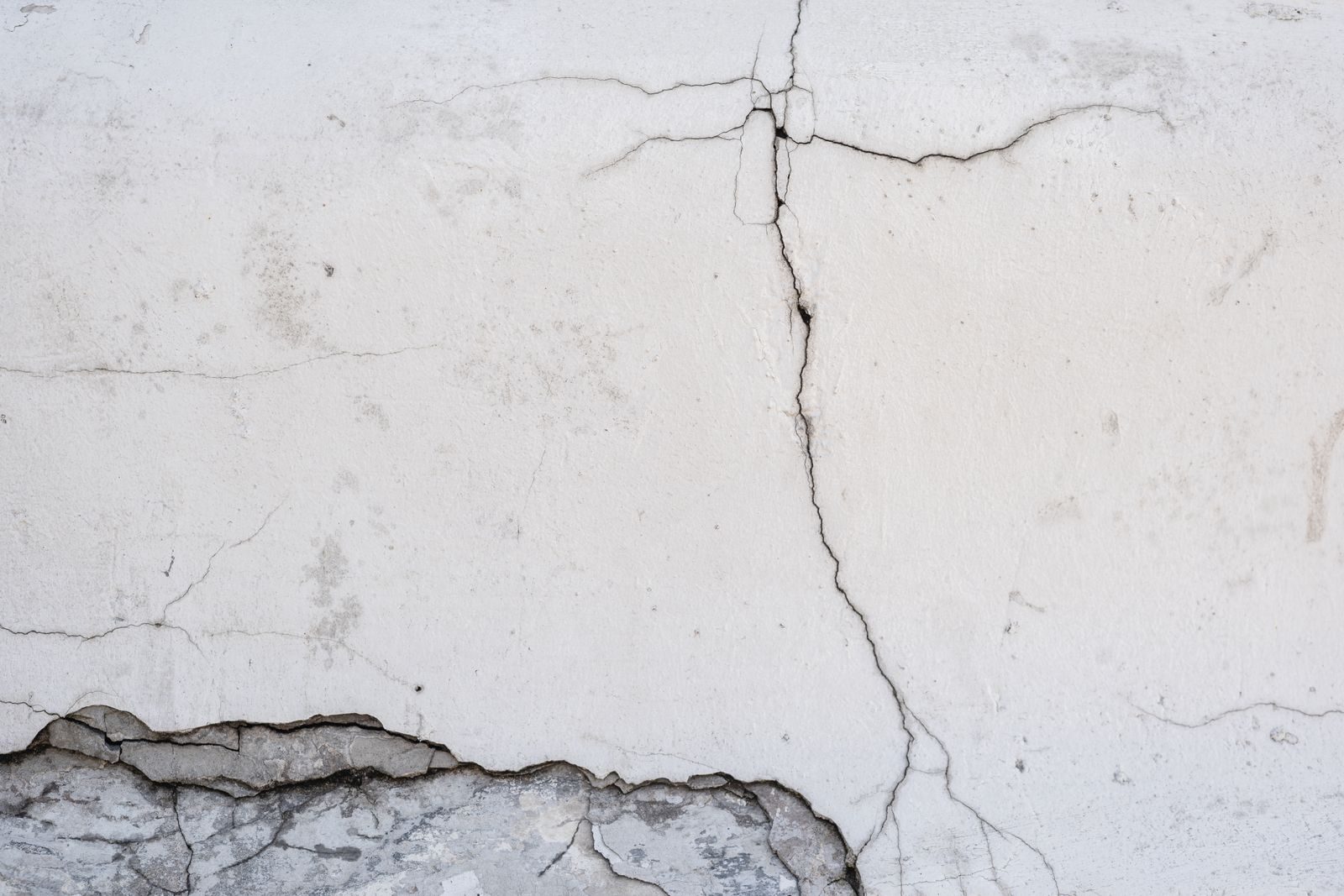 A vertical crack running down painted render, with a horizontal crack crossing it.