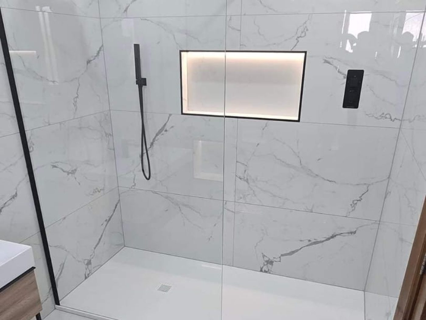 A walk-in shower built by GS Renovation, tiled in large format porcelain with a lit recess