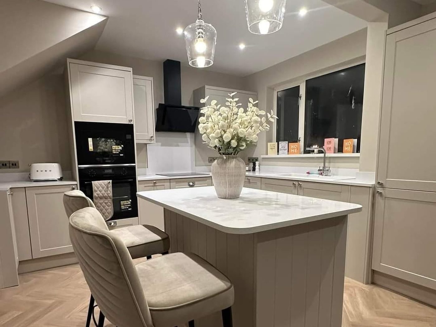 A cashmere shaker kitchen installed by GS Renovation with a stone-topped island and herringbone flooring