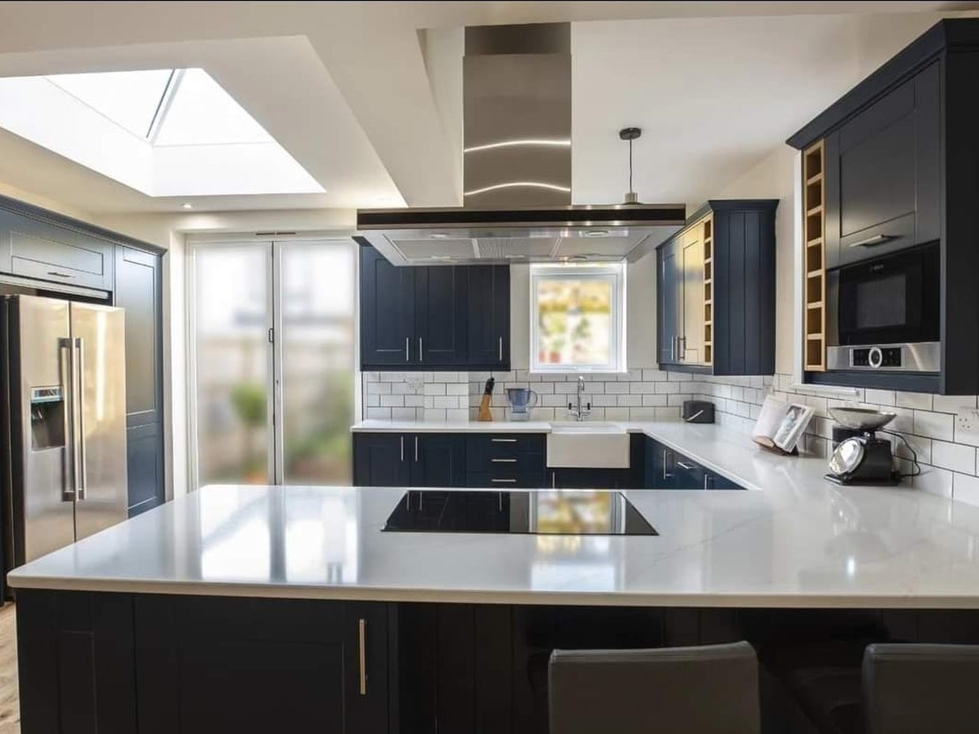 A navy shaker kitchen installed by GS Renovation with a stone peninsula, Belfast sink and a roof lantern above