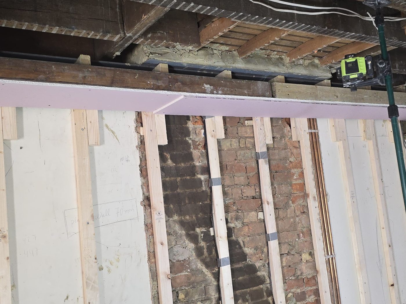 A steel beam being encased in fire-rated plasterboard by GS Renovation, with a laser level set up alongside